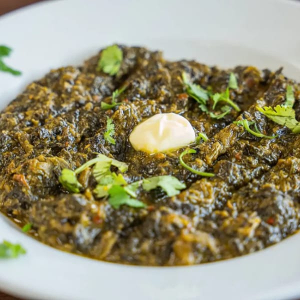 A white bowl filled with green saag, garnished with cilantro and a dollop of butter.