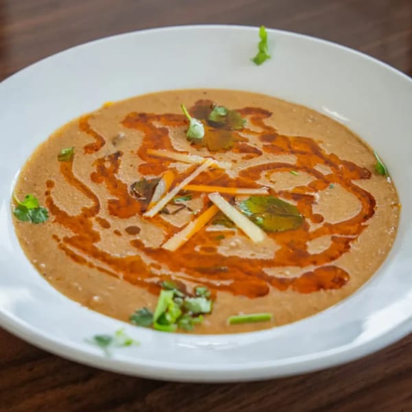 A white bowl of haleem, garnished with cilantro, ginger, and a swirl of chili oil.