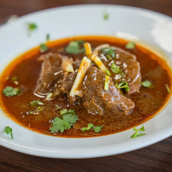 A white bowl filled with a rich, dark brown stew, garnished with fresh green cilantro.