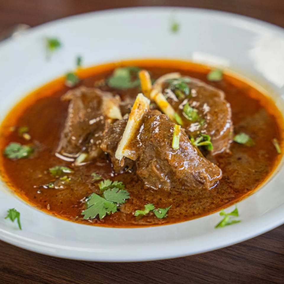 A white bowl filled with a rich, dark brown stew, garnished with fresh green cilantro.