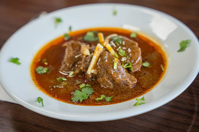 A white bowl filled with a rich, dark brown stew, garnished with fresh green cilantro.