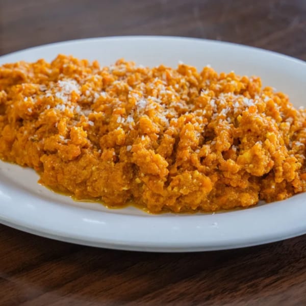 A white plate holds a serving of bright orange mashed sweet potatoes, sprinkled with white flakes.