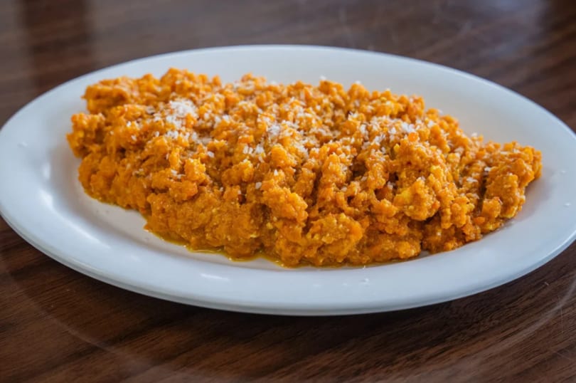 A white plate holds a serving of bright orange mashed sweet potatoes, sprinkled with white flakes.