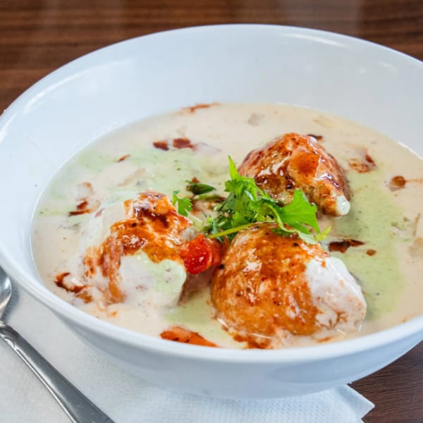 Dahi Vada, a popular Indian snack, served in a white bowl with a spoon on the side.